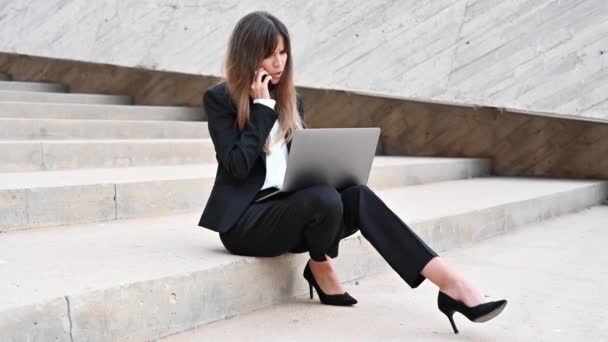 Angry Business woman having a phone call outdoors while working on laptop. Annoyed person talking on mobile phone, at office building stairs. Businesswoman arguing in phone conversation - Footage, Video