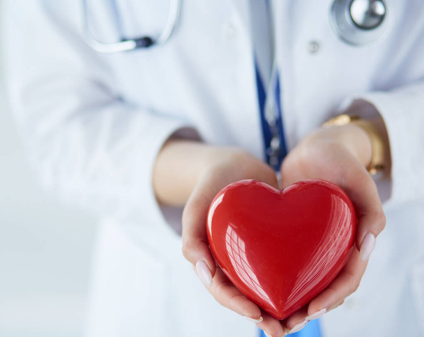Female doctor with stethoscope holding heart, on light background - 写真・画像
