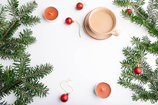 クリスマスや新年のフレーム構成。装飾、赤いボール、モミやトウヒの枝、コーヒーのカップ、白い紙の背景にキャンドル。トップビュー、コピースペース、フラットレイアウト. - 写真・画像