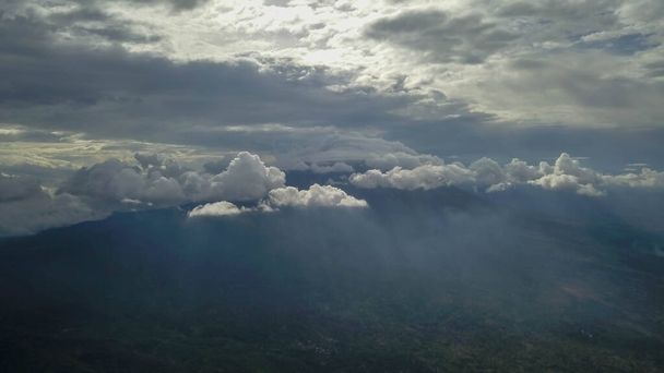 Vulkan mit wolkenlosem Himmel. Der Merapi in Indonesien. Bewölkter Himmel mit einem Vulkan im Hintergrund. Wolken rund um den Gipfel des Berges. Die Sonnenstrahlen scheinen durch die Wolken. - Foto, Bild