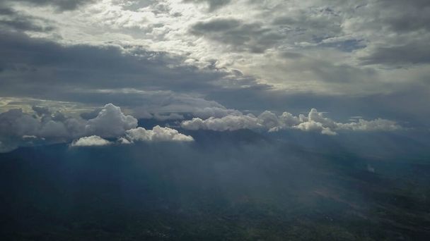 вулкан с облачно чистым небом. Гора Мерапи в Индонезии. Облачное небо на фоне вулкана. Облака вокруг вершины горы. Солнечные лучи светят сквозь облака. - Фото, изображение