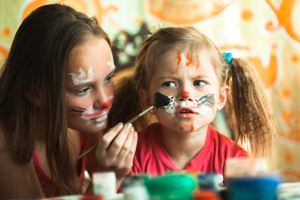 Kleine grappige zusjes spelen met het schilderen van het gezicht. - Foto, afbeelding
