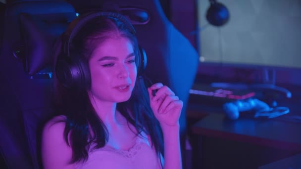 Fiatal nő ül a neon játék klub - visel nagy fejhallgató és beszél mikrofonban - Felvétel, videó