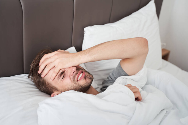 Man lying on the bed and feeling strong headache - Valokuva, kuva