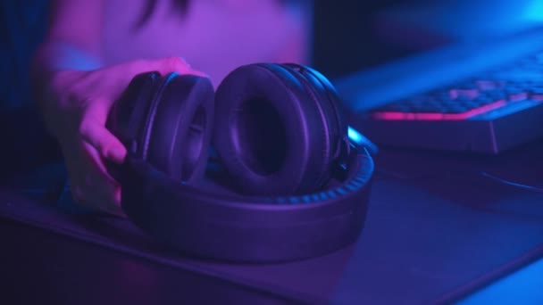 Young woman sitting in neon gaming club and putting on big headphones - looking in the camera - Footage, Video