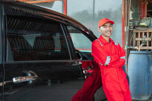 asian car washer in red uniform standing smiling leaning against the car - Foto, Bild