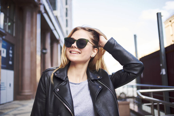 Happy woman model in a leather jacket walks down the street - Photo, Image