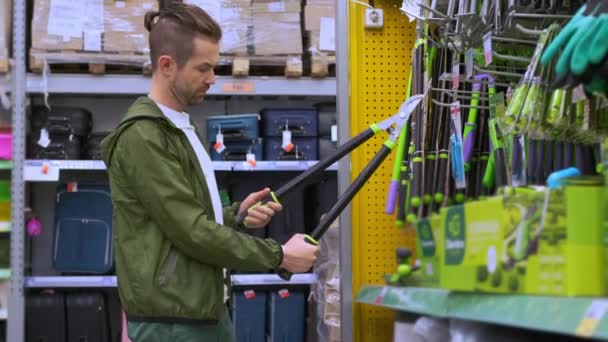 Молодой человек покупает большие садовые ножницы в гипермаркете - Кадры, видео