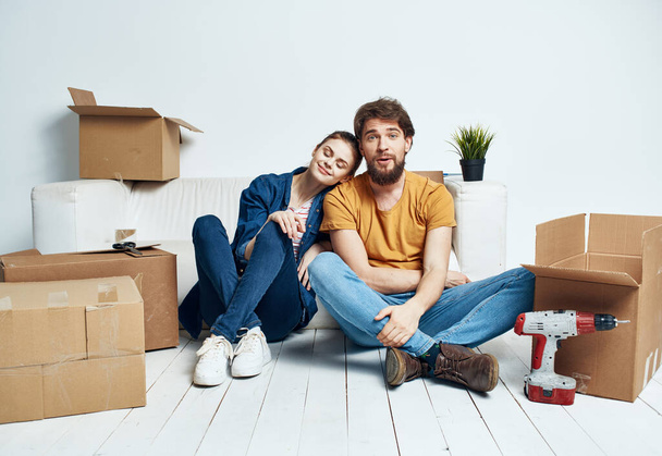 man and woman sitting on the floor with their backs to each other renovation work moving a flower in a pot - Photo, Image