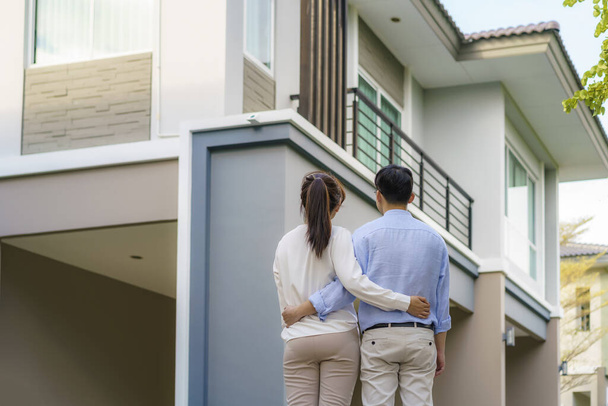 Portrait of Asian young couple standing and hugging together looking happy in front of their new house to start new life. Family, age, home, real estate and people concept. - Photo, Image