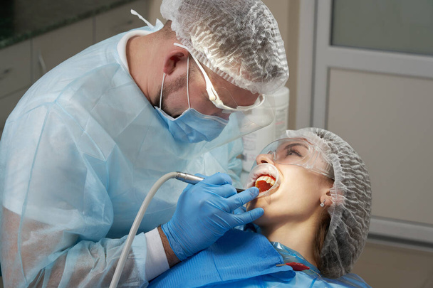 Tandarts doet een tandheelkundige behandeling bij een vrouwelijke patiënt. Tandarts onderzoekt een patiënt tanden in de moderne tandheelkunde kantoor - Foto, afbeelding