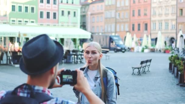 Обратный вид мужчины, делающего фотографии женщины-туристки на фоне городской рыночной площади - Кадры, видео