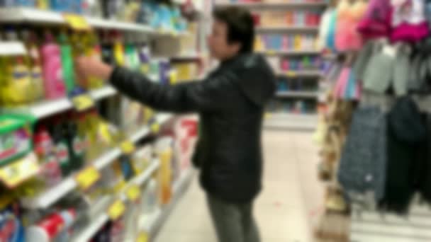 Iäkäs nainen valitsee ostoksia myymälässä kotitalouksien kemikaaleja ja kosmetiikkaa. 4k, hämärtynyt näkymä - Materiaali, video