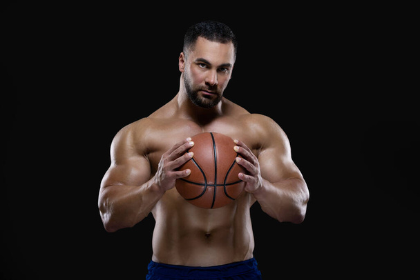 Front view portrait of an attractive sportsman holding a basketball with both hands isolated on black background - Fotoğraf, Görsel