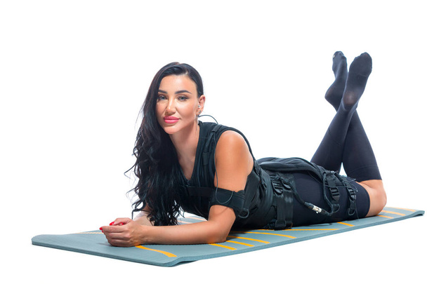 A young athletic woman in an EMS suit does lies on a Mat on an isolated white background. EMS training. Electrical muscle stimulator. - Фото, зображення