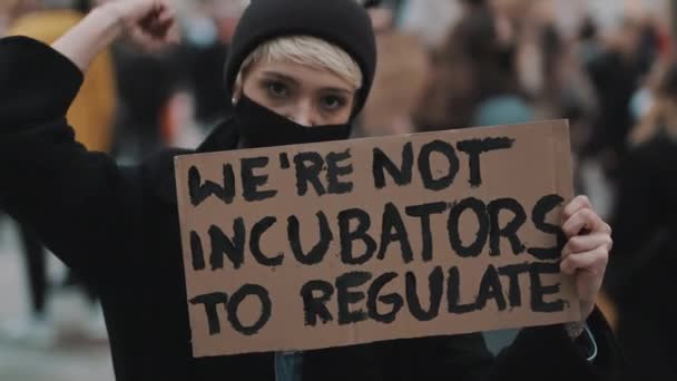 Marcha de mujeres. Mujer joven con máscara facial protestando con pancarta - No somos incubadoras para regular. protesta contra las estrictas leyes de aborto - Metraje, vídeo