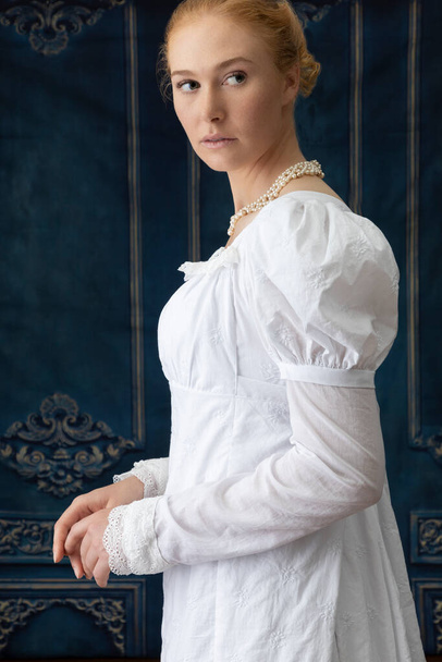 Una mujer de regencia vistiendo un vestido de muselina blanca y de pie en una habitación - Foto, Imagen