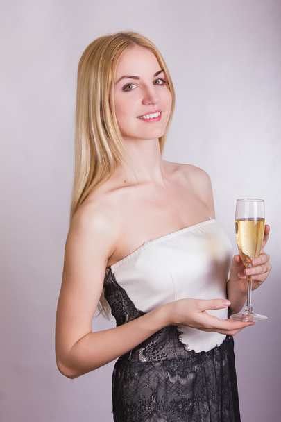 Ritratto di una bella giovane donna bionda su sfondo bianco in un abito corto bianco con pizzo nero. Ragazza carina in posa con un bicchiere di champagne nelle sue mani
. - Foto, immagini