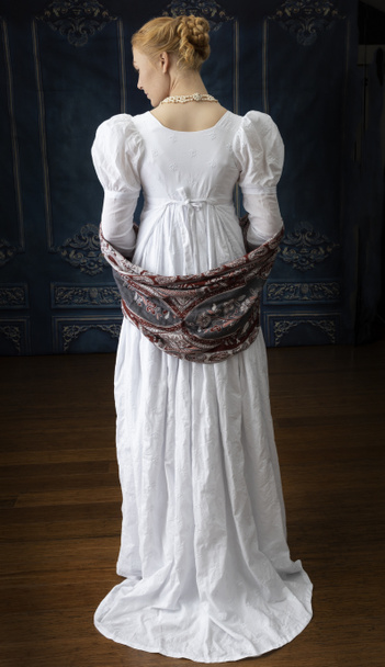 Een regentschap vrouw in een witte muslin jurk staand in een kamer - Foto, afbeelding