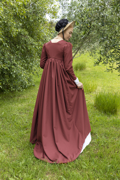 Una mujer de la Regencia con un vestido de muselina blanca, un largo separador, y un capó en un jardín. - Foto, imagen