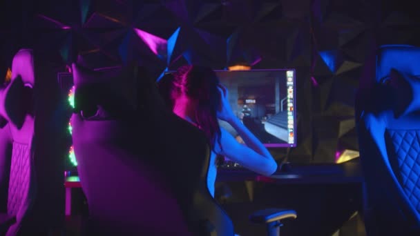 Młoda ładna kobieta siedzi w neonowym klubie gier i gra w gry - wstaje z krzesła i odchodzi - Materiał filmowy, wideo