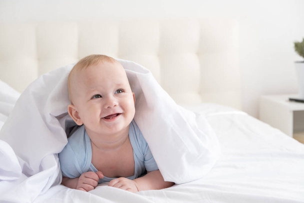 divertente bambino sorridente e sdraiato su un letto bianco a casa.  - Foto, immagini
