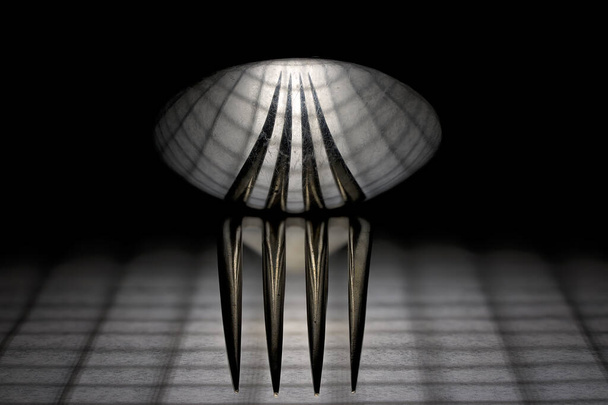 Une cuillère assise sur le dessus d'une fourchette reflétant le motif de grille ci-dessous, y compris les rayures sur les ustensiles - Photo, image