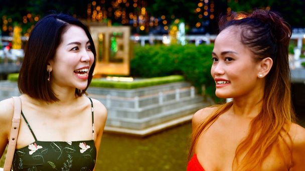 Две красивые молодые азиатские женщины разговаривают и расслабляются прогуливаясь по улицам города. - Фото, изображение