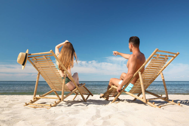 Woman in bikini and her boyfriend on deck chairs at beach. Lovely couple - Foto, Imagen