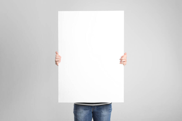 Man holding blank poster on light grey background - Foto, afbeelding