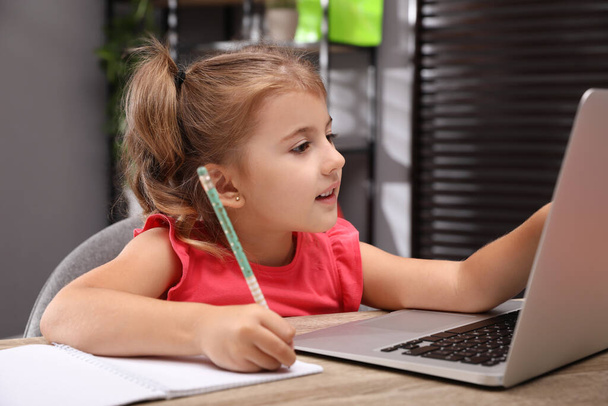 Nettes kleines Mädchen macht Hausaufgaben mit Laptop am Tisch - Foto, Bild