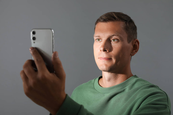 Man unlocking smartphone with facial scanner on grey background. Biometric verification - Photo, Image