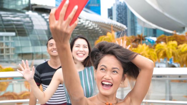 Τρεις νέοι ασιάτες φίλοι απολαμβάνουν υπαίθριο χρόνο λαμβάνοντας selfies κατά μήκος των δρόμων της πόλης. - Φωτογραφία, εικόνα