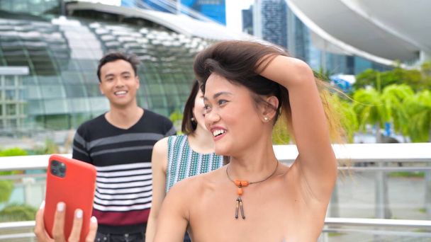 tres asiático jóvenes amigos disfrutar al aire libre tiempo tomando selfies a lo largo de la ciudad calles. - Foto, Imagen