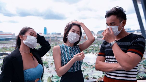 Tres asiáticos jóvenes amigos de pie al aire libre en la ciudad hablando y usando mascarillas en covid coronavirus pandemia. - Foto, imagen