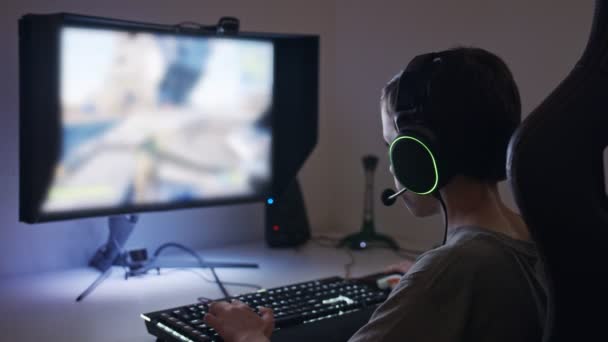 Fiatal fiú ül a számítógép előtt, játszani egy játékot visel egy headset - Felvétel, videó