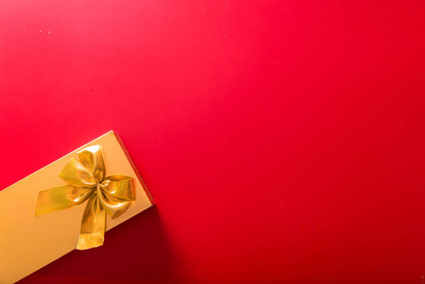 Lahja kultaisessa paketissa, jossa on rusetti punaisella taustalla. Vaakasuora kuva - Valokuva, kuva