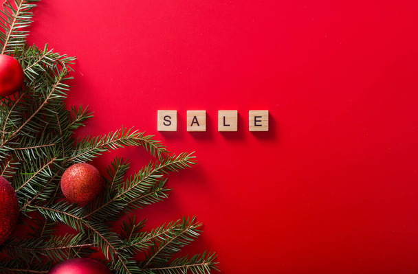 Christmas trees with red balls and the word SALE made of wooden letters on a red background. Top view. Seasonal sale. Horizontal photo - Fotografie, Obrázek