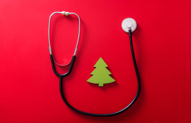 Stetoskooppi ja käsintehty lelu pieni joulukuusi punaisella taustalla. Yläkuva - Valokuva, kuva