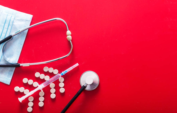 Spuit, pillen, masker en stethoscoop op een rode achtergrond. Horizontale foto - Foto, afbeelding