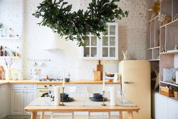 Light kitchen in the style of loft, preparation for the holiday, served table, a large evergreen branch of spruce - Φωτογραφία, εικόνα