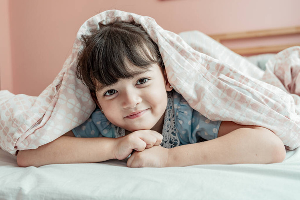Chica alegre divirtiéndose debajo de la manta en el dormitorio. - Foto, Imagen