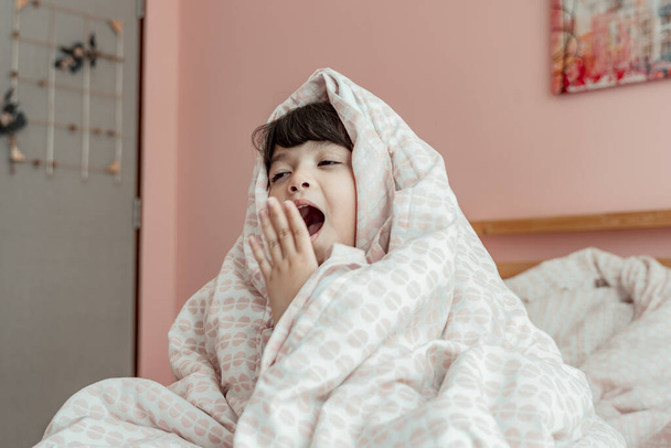 Adorable little girl wrapped in soft blanket yawning expression. - Photo, Image