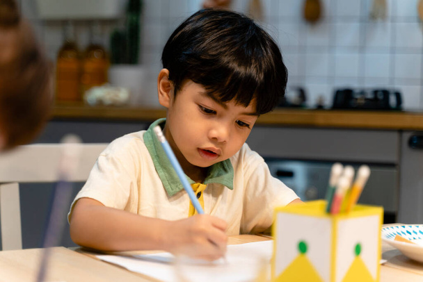 Маленький мальчик делает домашнюю работу за столом на кухне. - Фото, изображение