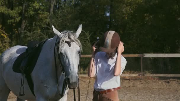 若い女性は彼女の馬に乗るために準備,彼女は乗馬ヘルメットを置きます - 映像、動画