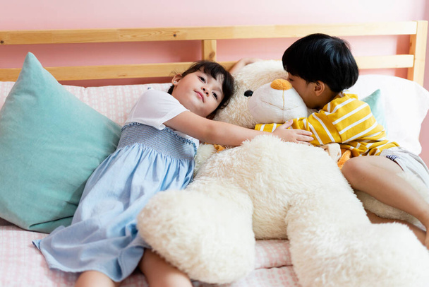 Fratello e sorella abbracciare morbidamente grande orso bambola insieme in camera da letto. - Foto, immagini