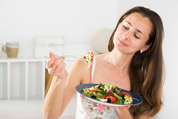 Positive pretty woman holding fork and eating vegetable salad in bed - 写真・画像