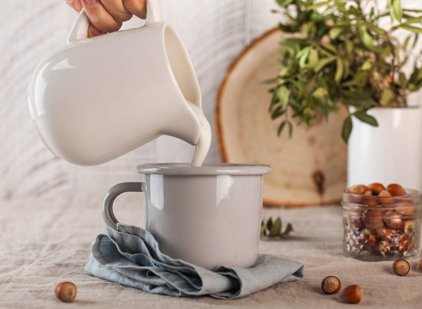 Milk is poured from a white jug into a mug. Food photos in rustic style. Concept of farm products. High quality photo - Foto, Bild