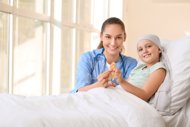 Νοσοκόμα και κοριτσάκι με χρυσή κορδέλα στην κλινική. Έννοια ευαισθητοποίησης για τον καρκίνο του παιδιού - Φωτογραφία, εικόνα