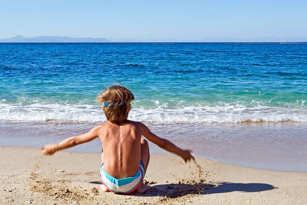 de jongen gooit zand op het strand - Foto, afbeelding
